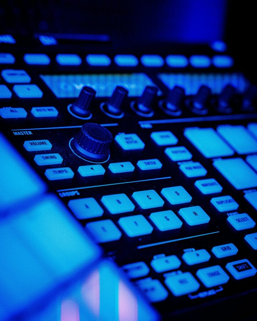 Équipement de beatmaking et production musicale éclairé par des néons bleus, avec un contrôleur MIDI moderne et des boutons lumineux.