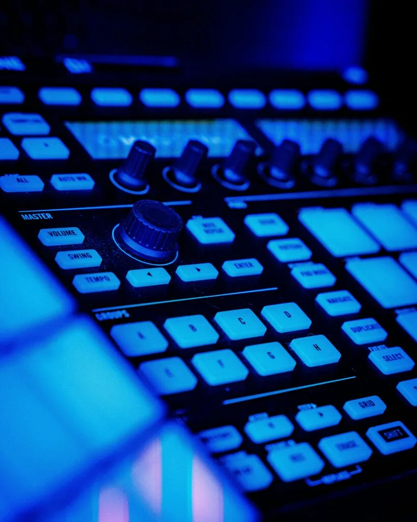 Équipement de beatmaking et production musicale éclairé par des néons bleus, avec un contrôleur MIDI moderne et des boutons lumineux.