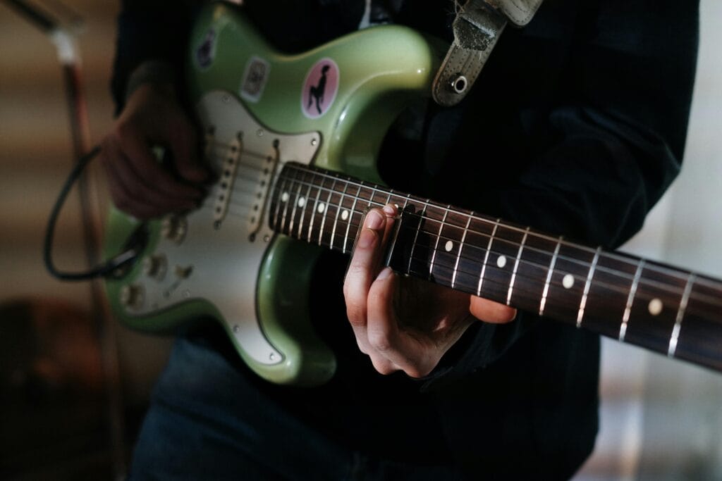 Plan rapproché des mains d’un musicien jouant sur une guitare électrique verte à l’intérieur.