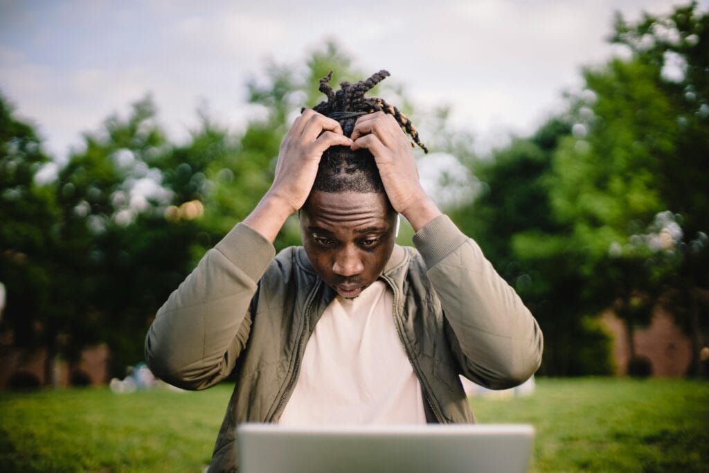 Jeune homme afro-américain contrarié assis à l’extérieur dans un parc