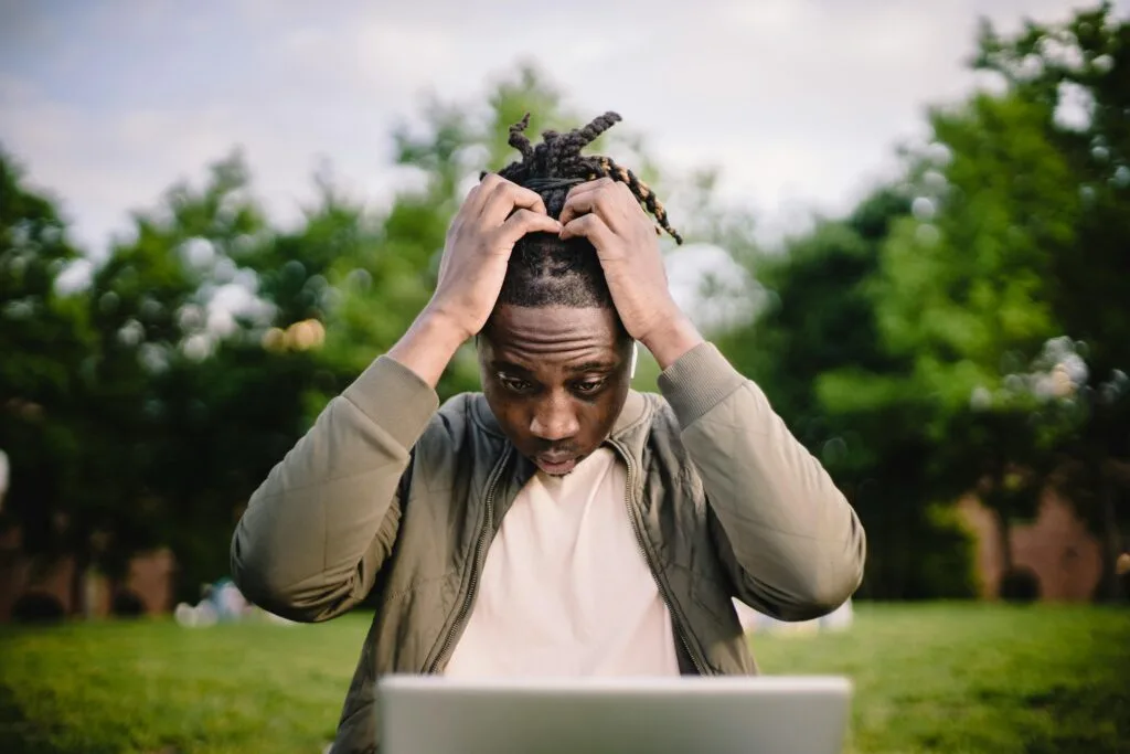 Jeune homme afro-américain contrarié assis à l’extérieur dans un parc
